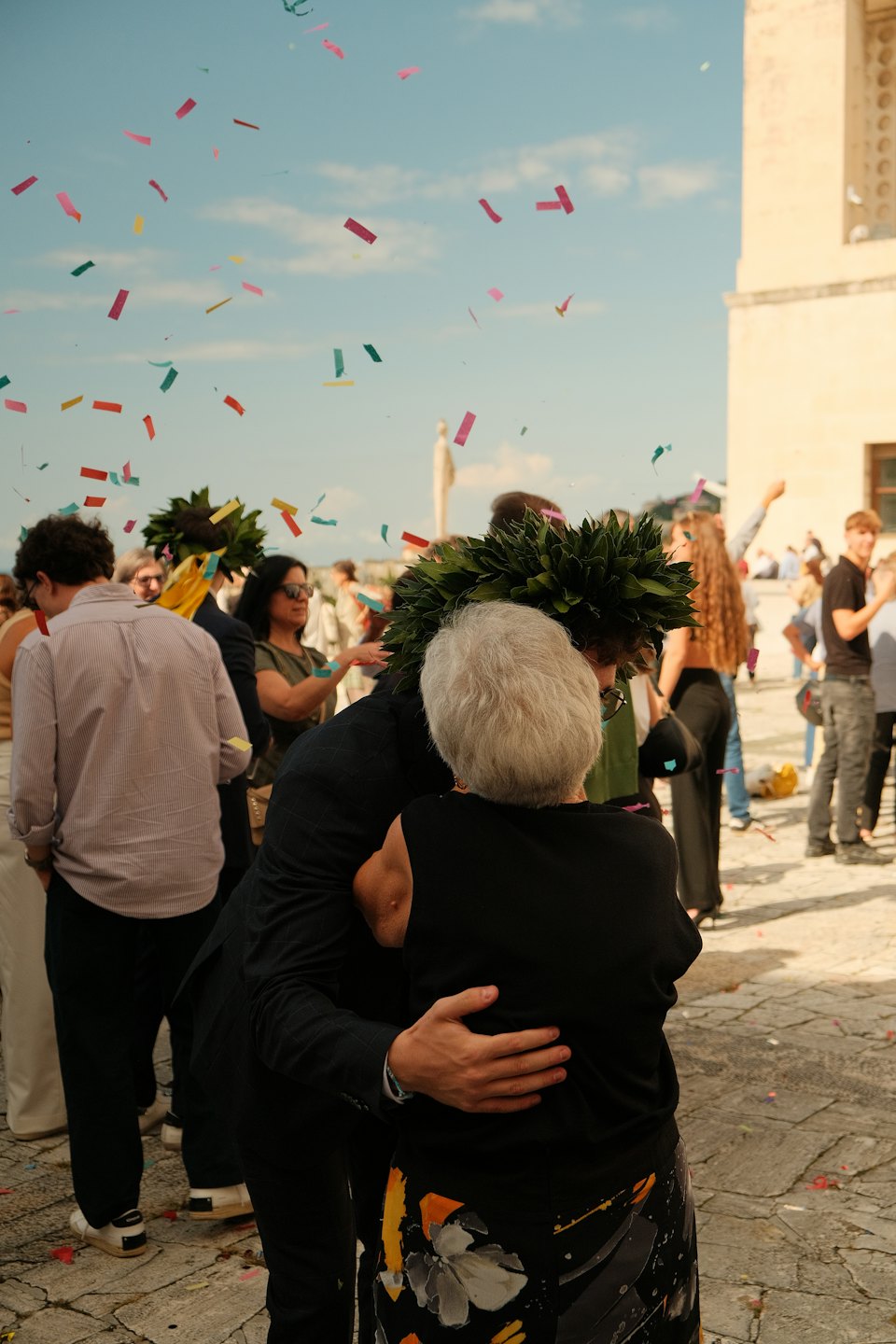 Two people embrace outdoors while confetti falls around them.