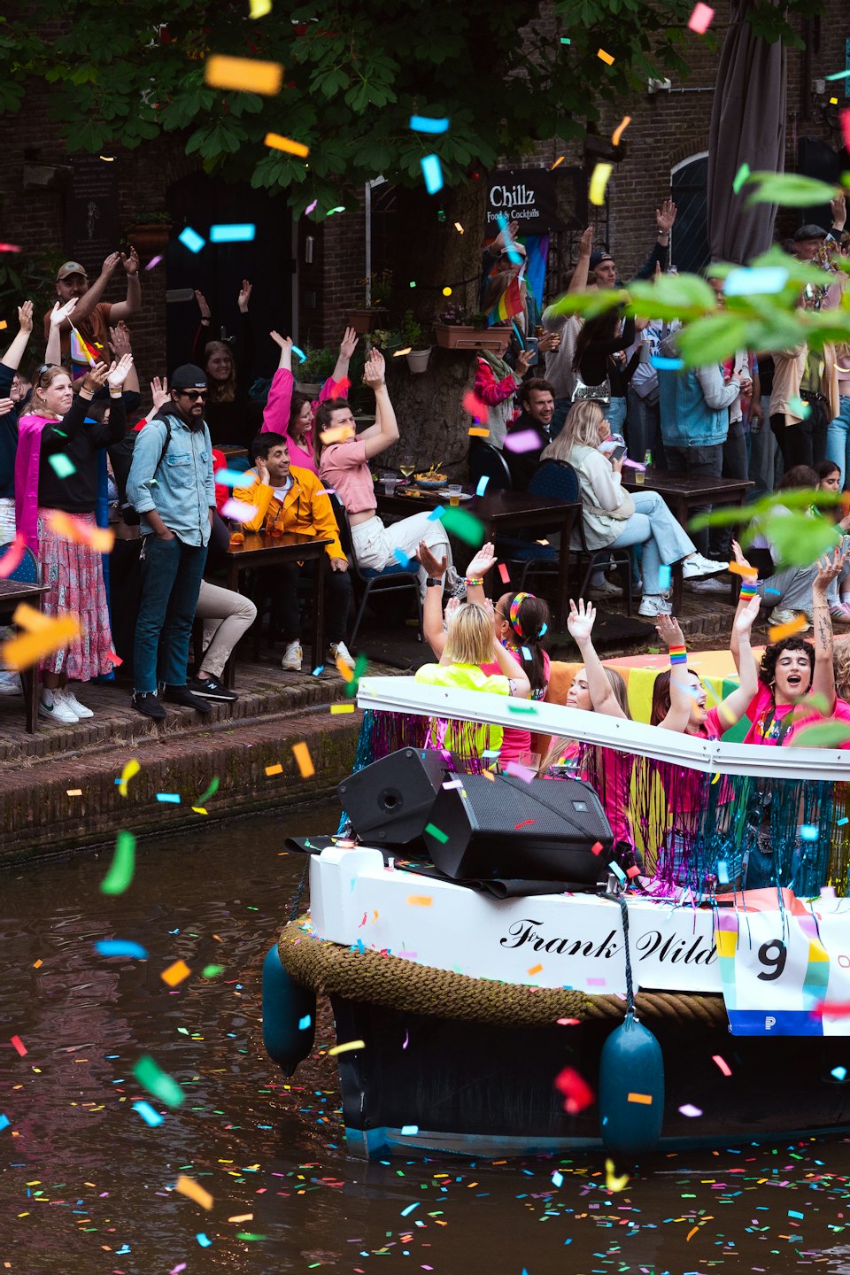 People celebrate on a decorated boat and canal bank with confetti.